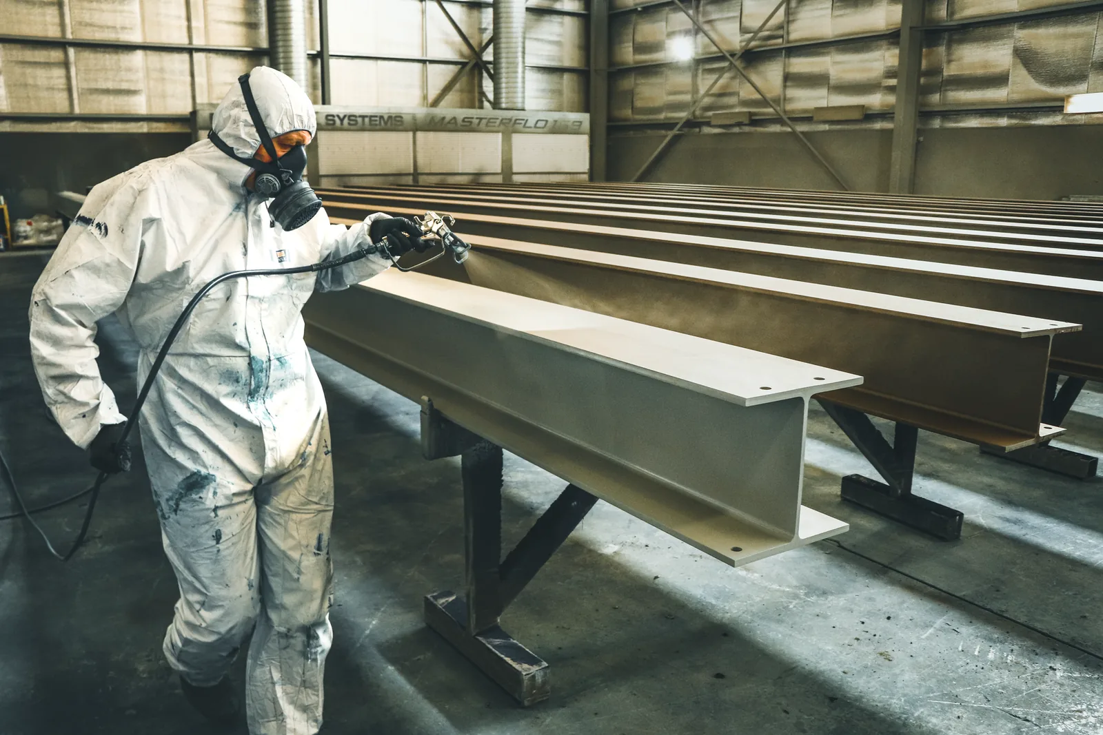 Industrial worker spray painting metal beams in factory